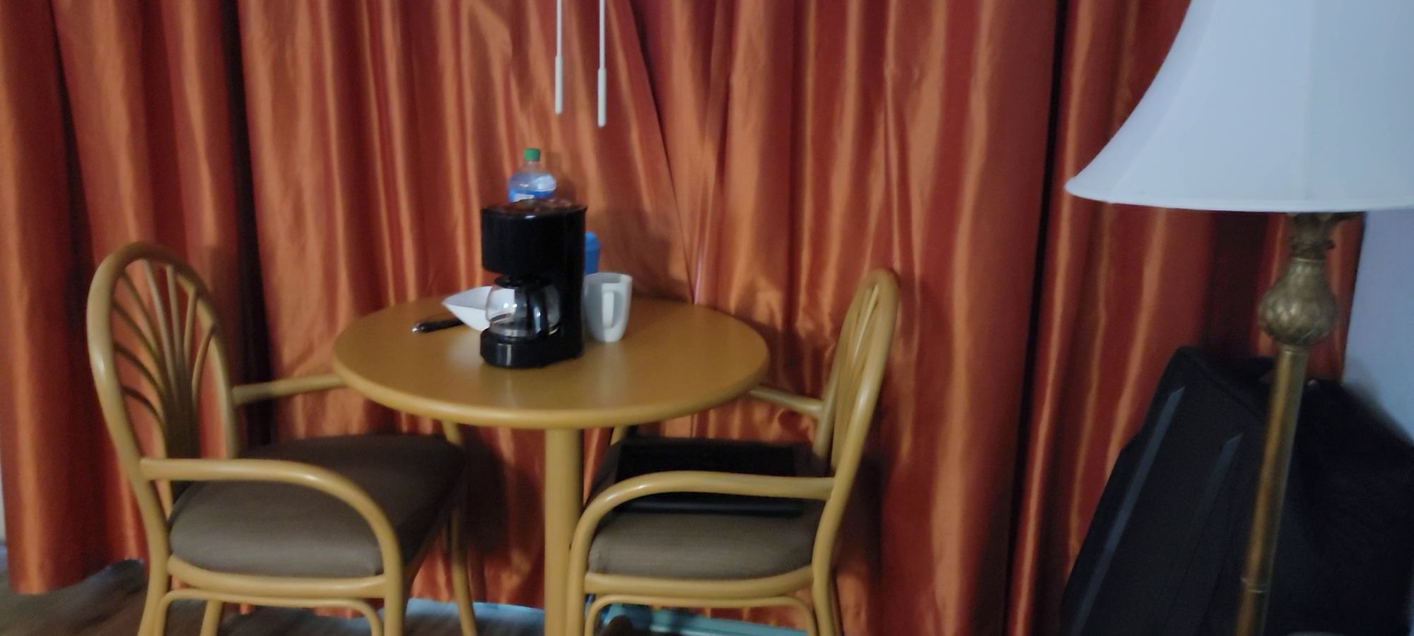 An image of a coffeepot sitting on a table, with two chairs and a lamp nearby